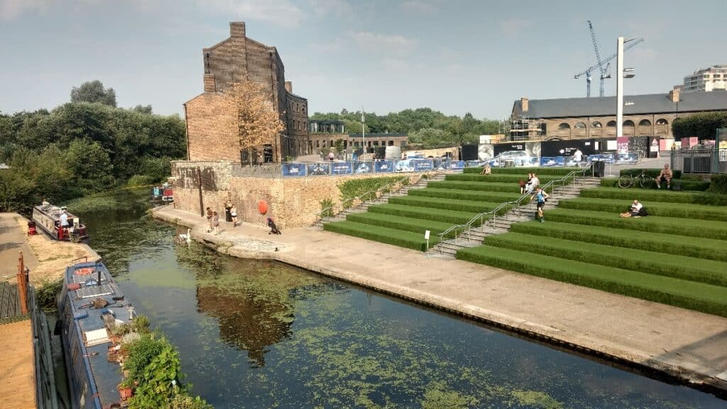 Industrial and recreational landscape with people sitting by a canal with cranes in the background